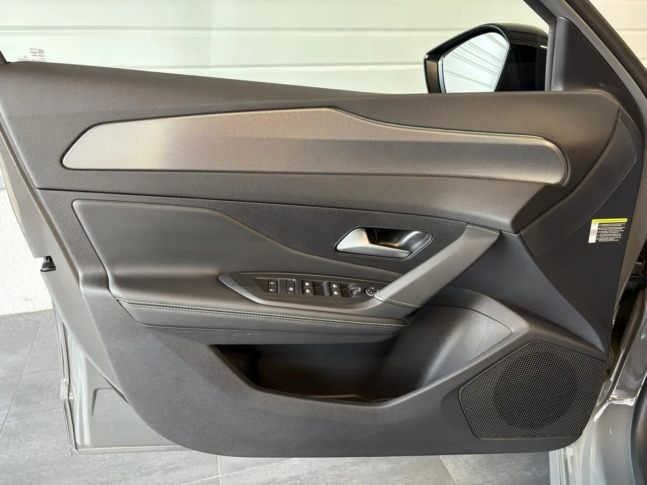 Porte avant gauche ouverte d'une Peugeot 308 gris selenium, montrant le panneau de porte avec commandes et finition noire élégante.