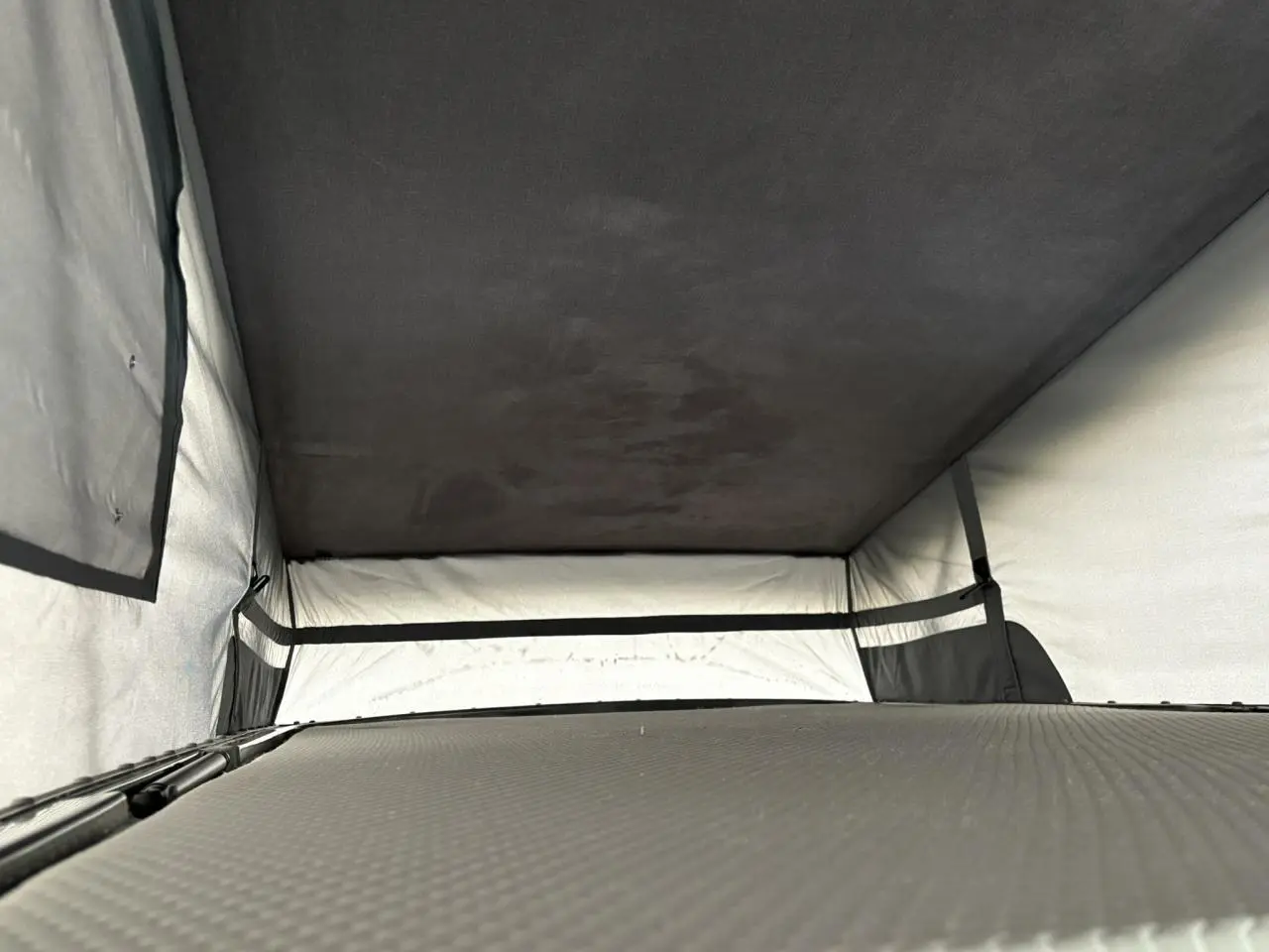 Intérieur du toit relevable du Volkswagen Transporter jaune et blanc, vue en plongée sur la couchette aménagée.