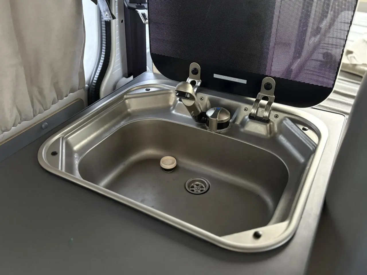 Gros plan sur l'évier en inox intégré dans l'aménagement intérieur du Volkswagen Transporter jaune et blanc.