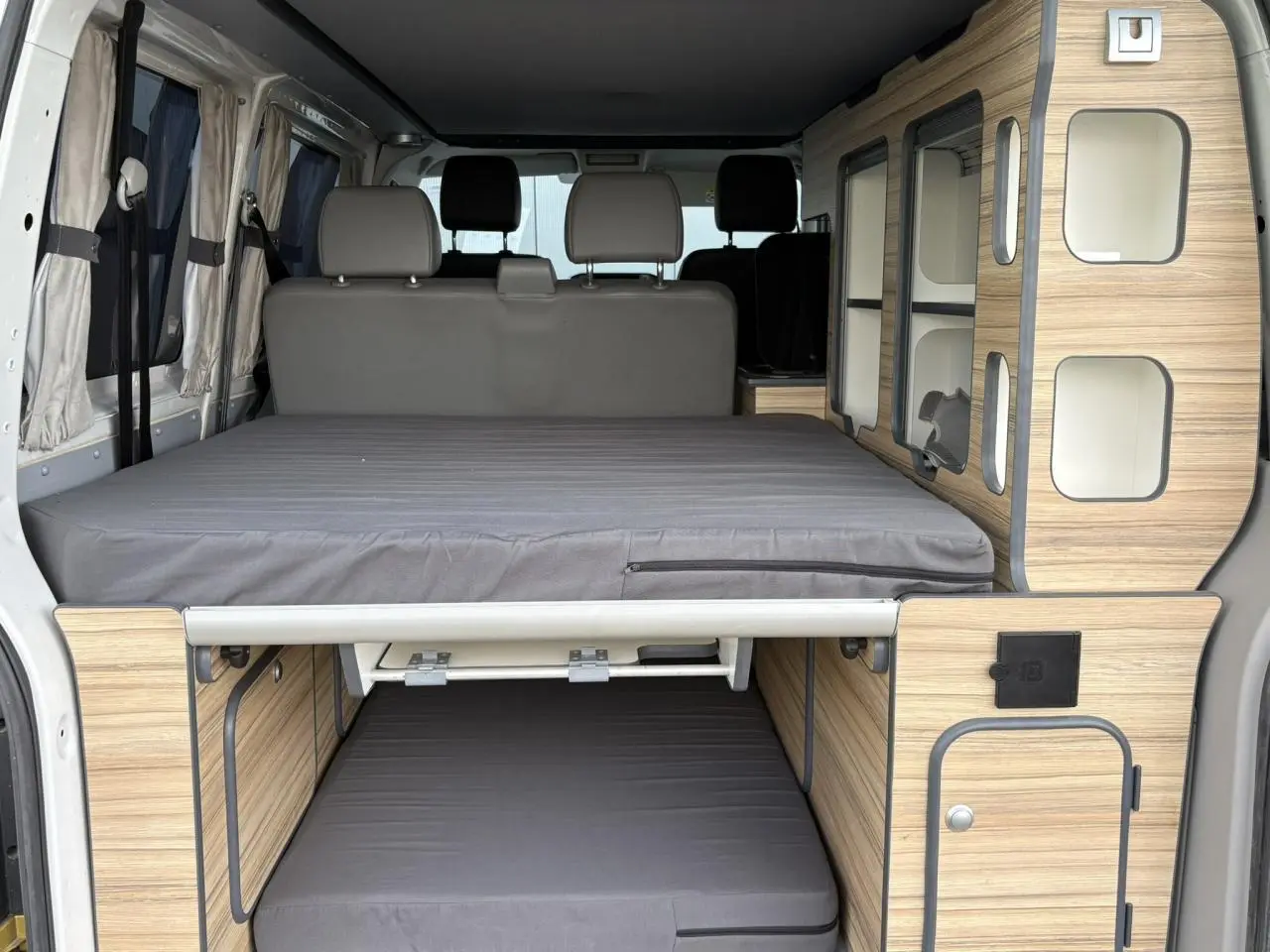 Vue arrière intérieure du Volkswagen Transporter aménagé avec lits superposés et mobilier bois clair.