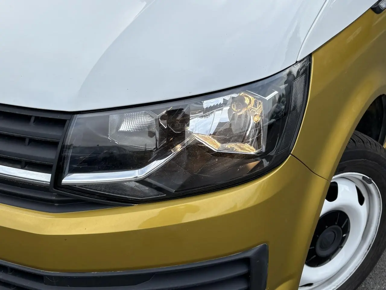 Gros plan sur le phare avant droit du Volkswagen Transporter 2.0 TDI jaune et blanc, mettant en valeur la calandre noire et la jante acier.