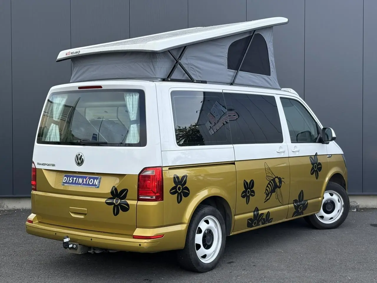 Vue 3/4 arrière droite du Volkswagen Transporter 2017 jaune et blanc avec toit relevé et décor floral noir sur la carrosserie.