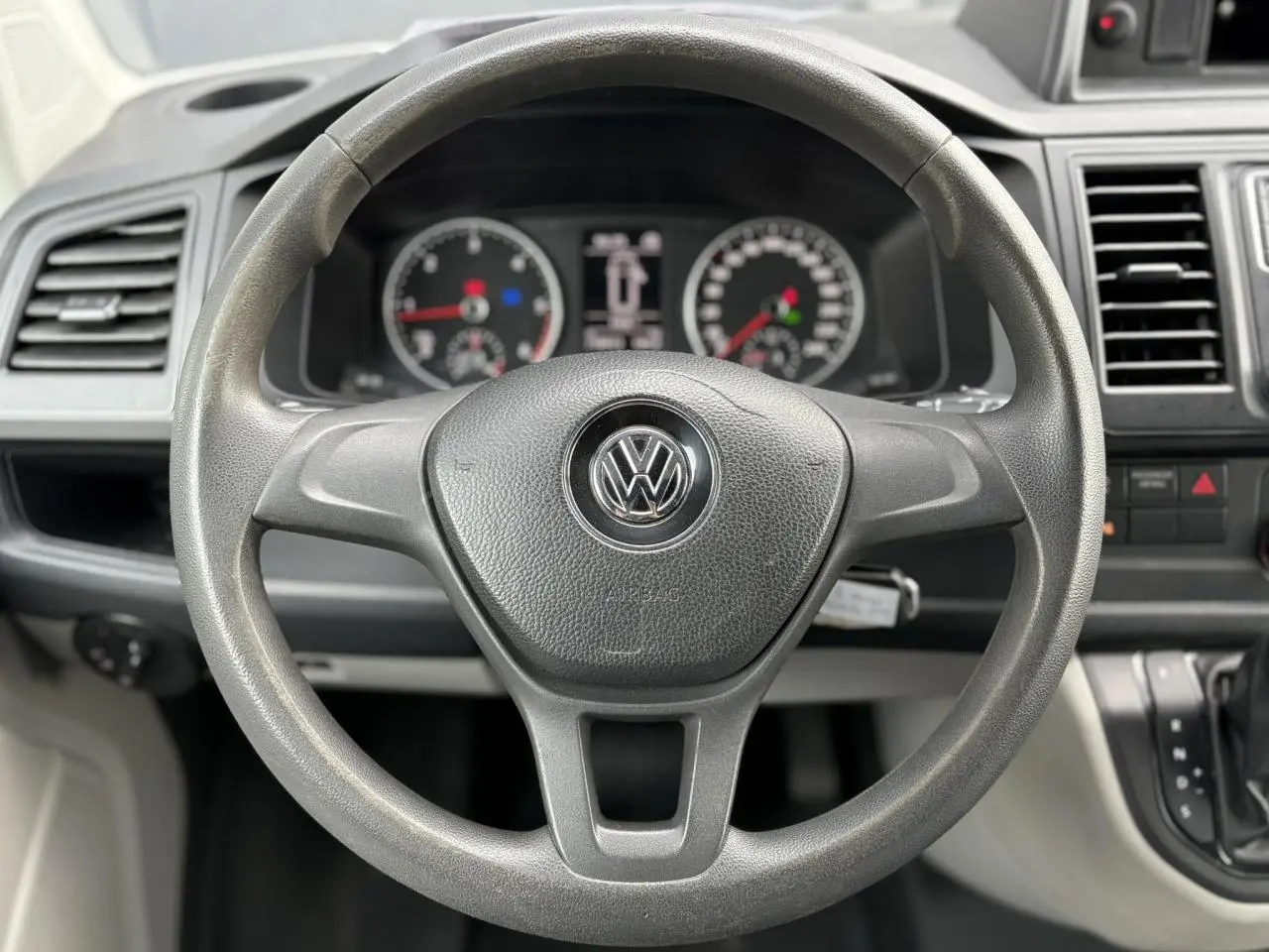 Volant noir avec logo Volkswagen au centre, tableau de bord et commandes du Volkswagen Transporter 2017 visibles en plan rapproché.