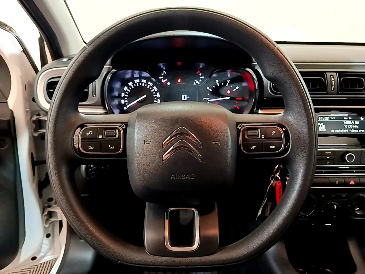 Vue centrée sur le volant noir de la Citroën C3 blanche, avec tableau de bord et commandes au volant visibles.