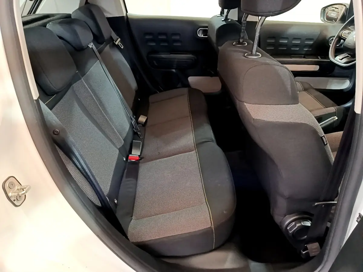 Vue intérieure côté gauche montrant la banquette arrière et l'avant de la Citroën C3 blanche avec sièges gris foncé.