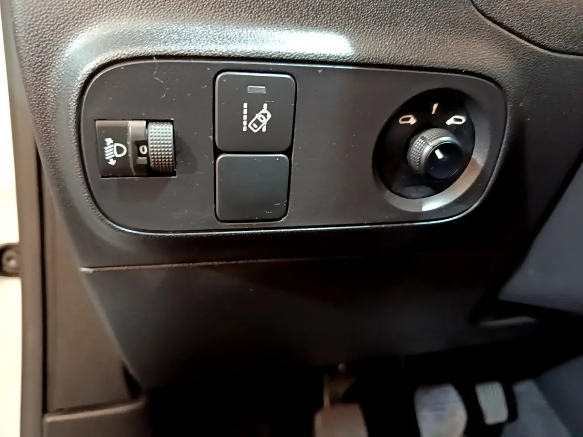 Gros plan sur les commandes de réglage des phares et des rétroviseurs côté conducteur d'une Citroën C3 blanche 2018.