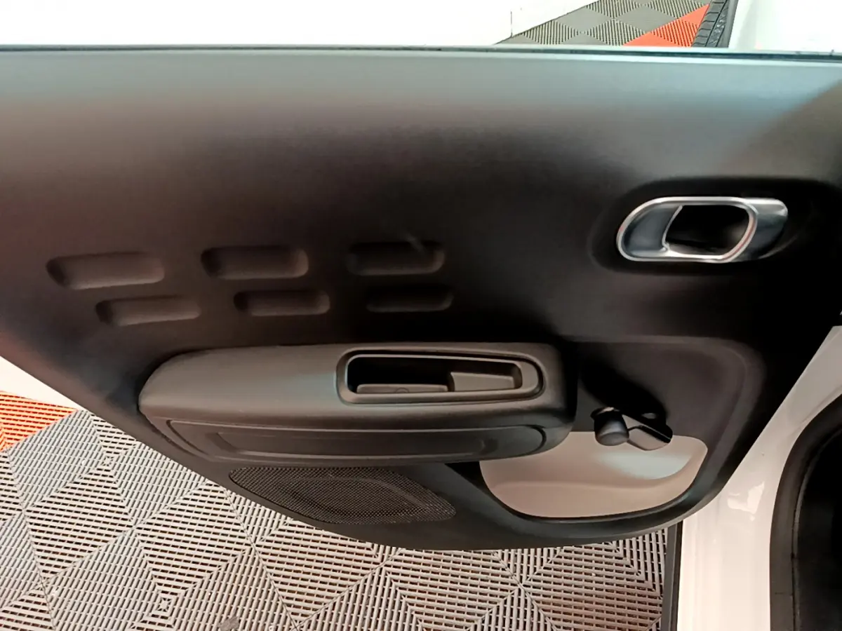 Vue rapprochée de la porte avant droite d'une Citroën C3 blanche, montrant la poignée intérieure et les commandes manuelles des vitres.