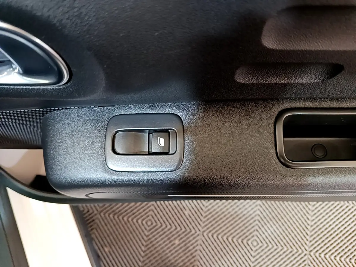 Gros plan sur le bouton de commande de la fenêtre côté conducteur d'une Citroën C3 blanche, intérieur noir.