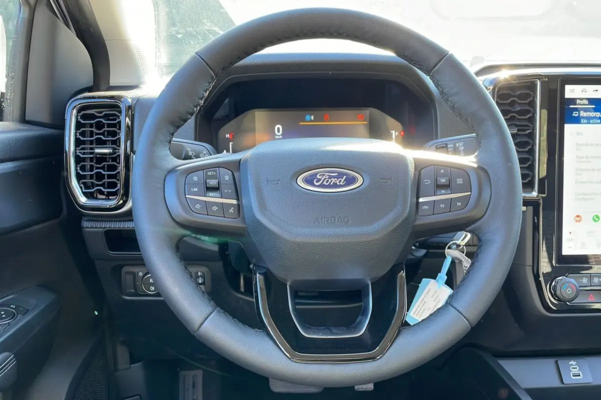 Vue rapprochée du volant en cuir noir du Ford Ranger 2025 gris iconic, avec commandes intégrées et tableau de bord digital.