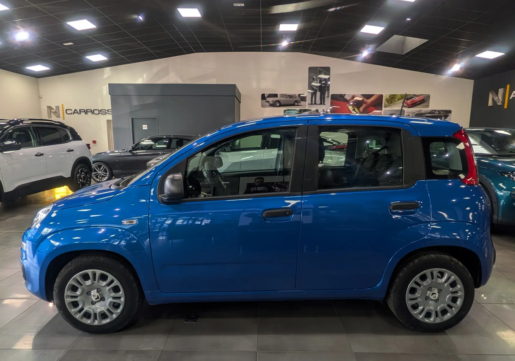 Profil côté gauche d'une FIAT Panda 1.0 Hybrid City 2025 en Bleu Italia, exposée en intérieur avec jantes acier.