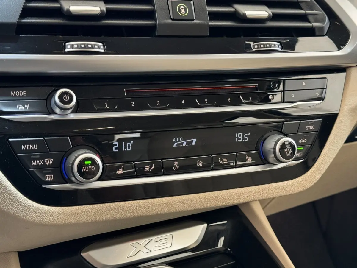 Gros plan sur la console centrale beige et noire du BMW X3 2018, avec commandes climatisation digitale et logo X3 visible.
