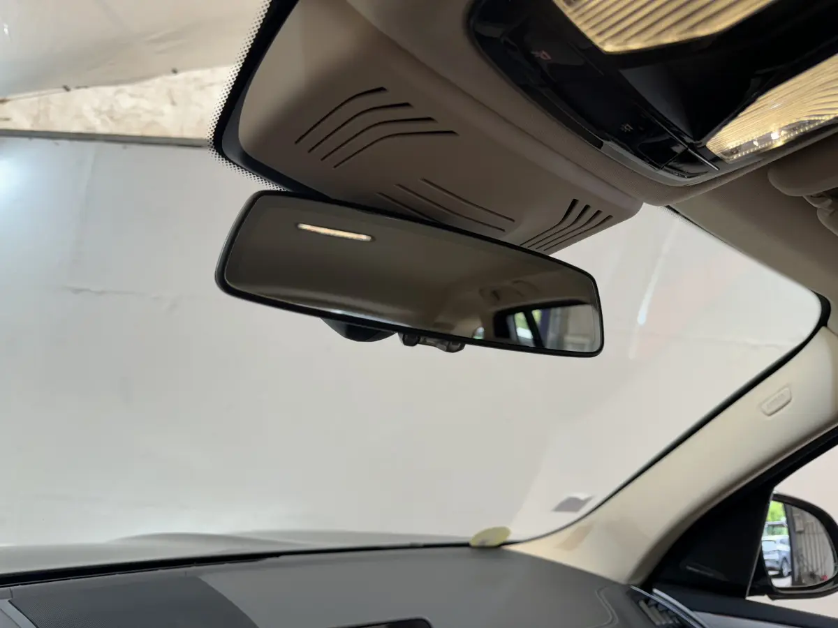 Vue intérieure centrée sur le rétroviseur intérieur d’un BMW X3 gris foncé, avec plafond beige et pare-brise visible.
