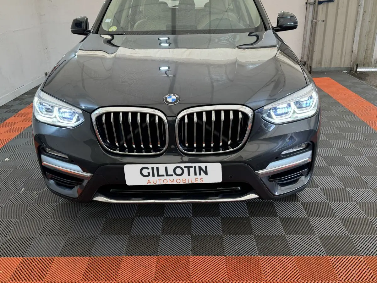Vue frontale d'une BMW X3 xDrive30d gris foncé avec phares LED allumés et calandre double haricot chromée.
