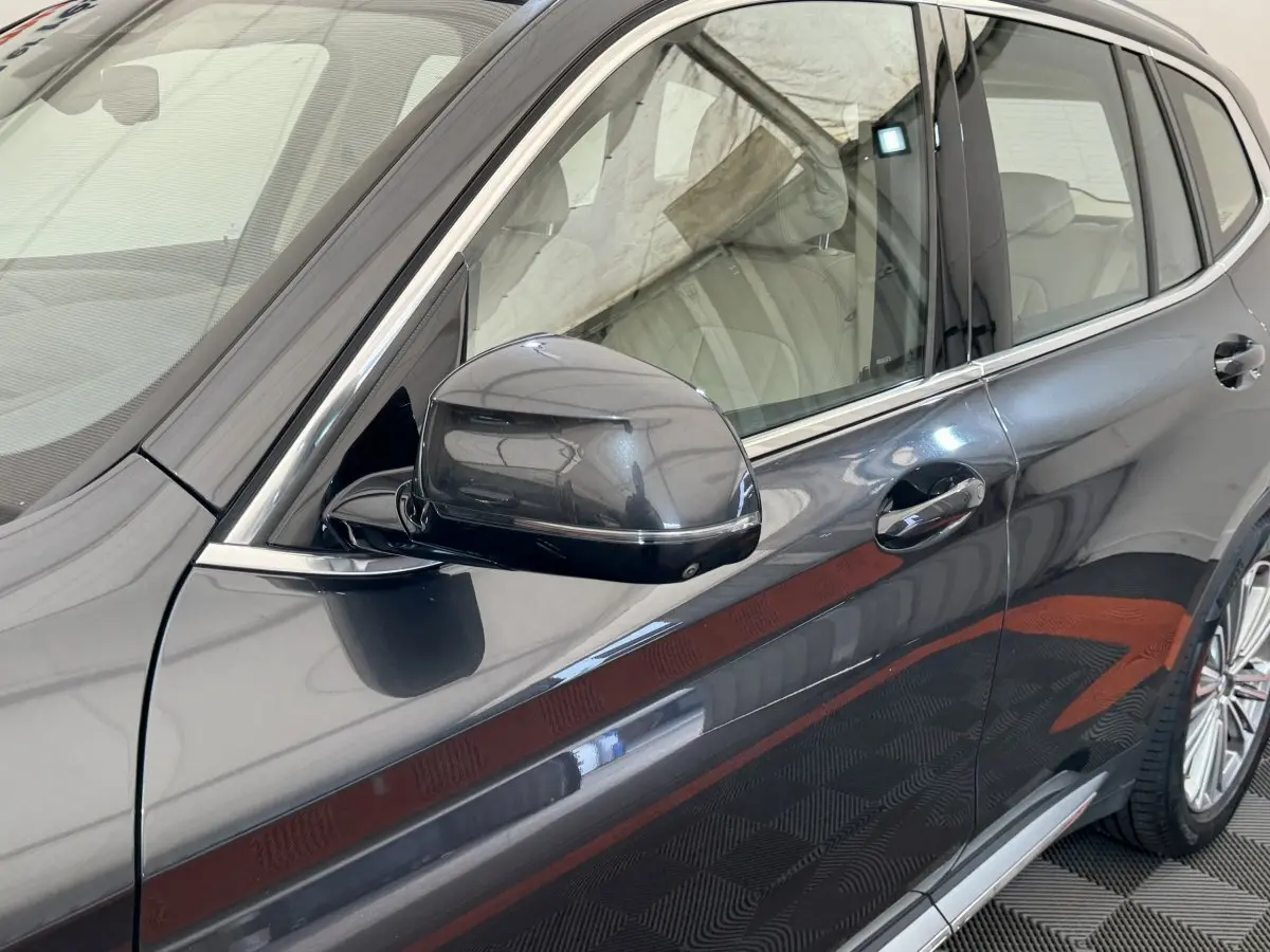 Vue rapprochée côté gauche d’un BMW X3 gris foncé 2018 avec rétroviseur et poignée de porte visibles.