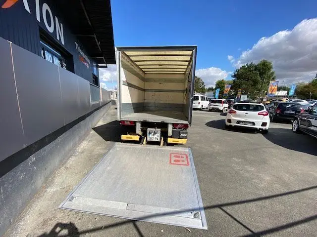 Vue arrière d'un Ford Transit Chassis Cabine jaune 2015 avec hayon déployé et caisse ouverte sur parking.
