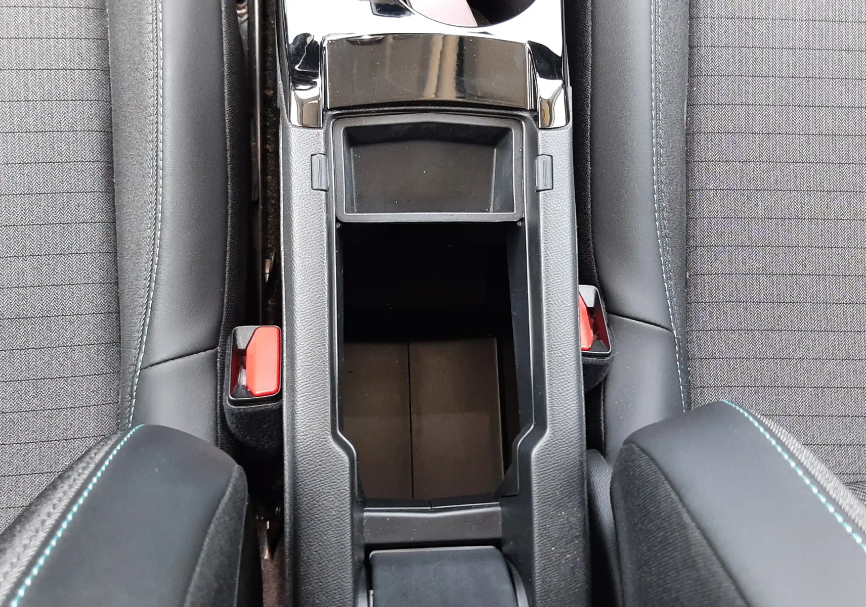 Vue plongeante sur la console centrale noire du Peugeot 2008 gris Artense, avec porte-gobelets et accoudoirs en tissu noir.