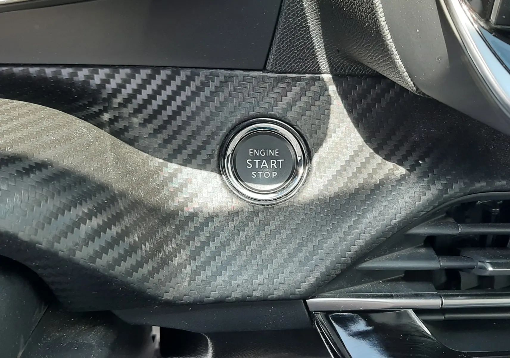 Bouton start/stop moteur sur tableau de bord avec finition carbone à l'intérieur d'un Peugeot 2008 gris Artense 2022.