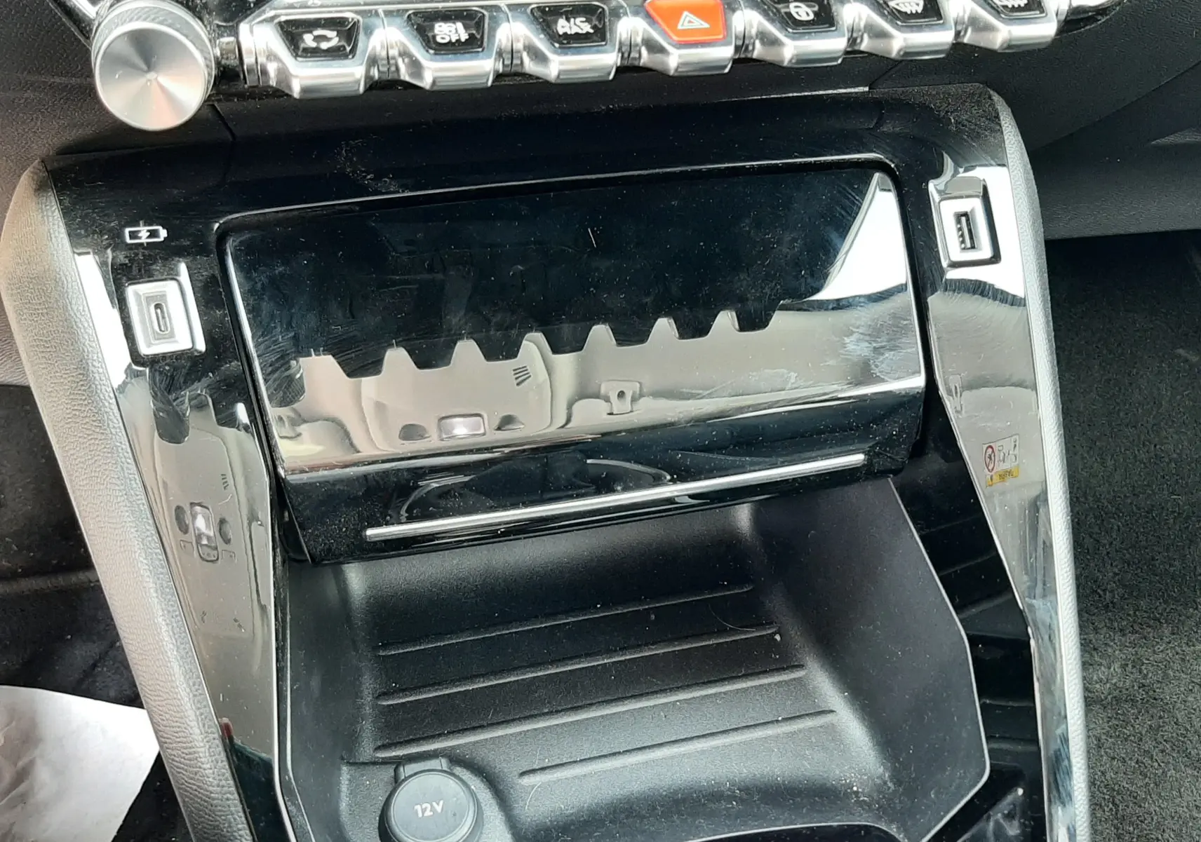 Gros plan sur la console centrale noire brillante du Peugeot 2008 2022, avec boutons de commande et prise 12V visible.