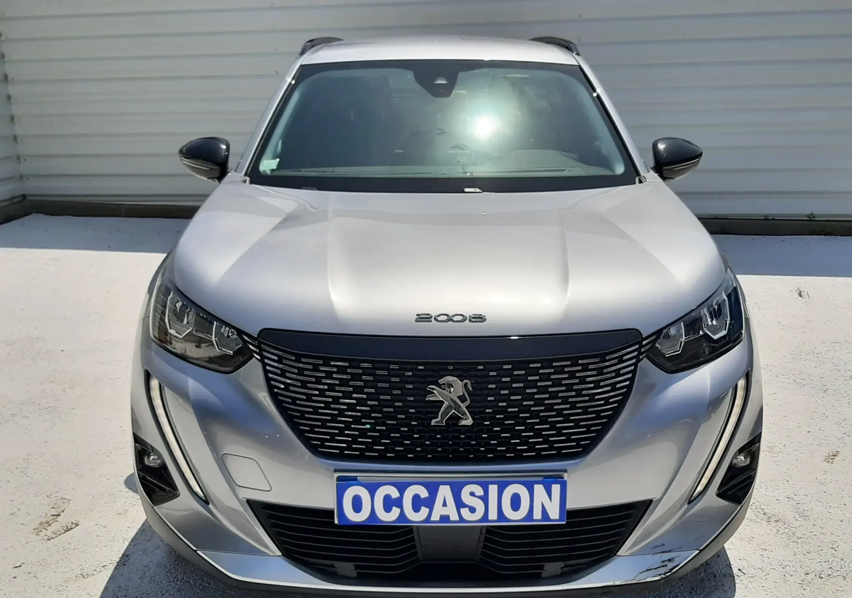 Vue avant d'un Peugeot 2008 gris Artense avec calandre noire et plaque "OCCASION" visible en extérieur.