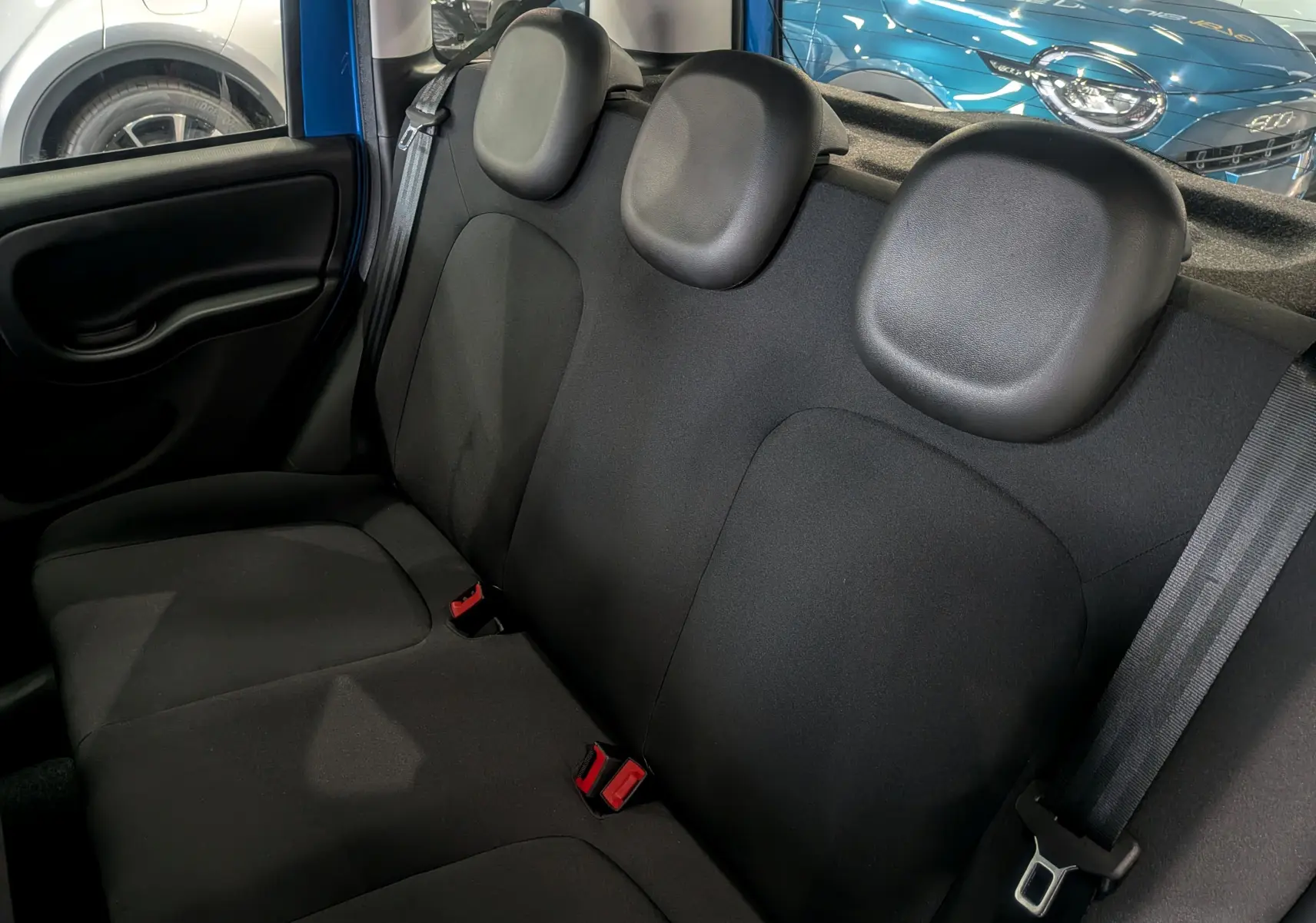 Vue intérieure du siège arrière en tissu noir de la Fiat Panda 2025 Bleu Italia, avec appuie-têtes et ceinture de sécurité visible.