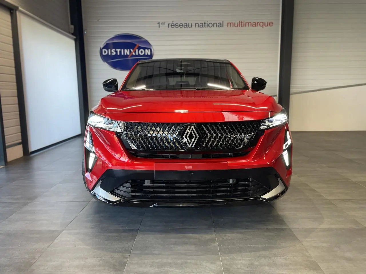 Vue frontale d'une Renault Rafale 2025 rouge avec calandre noire et feux LED allumés dans un showroom.