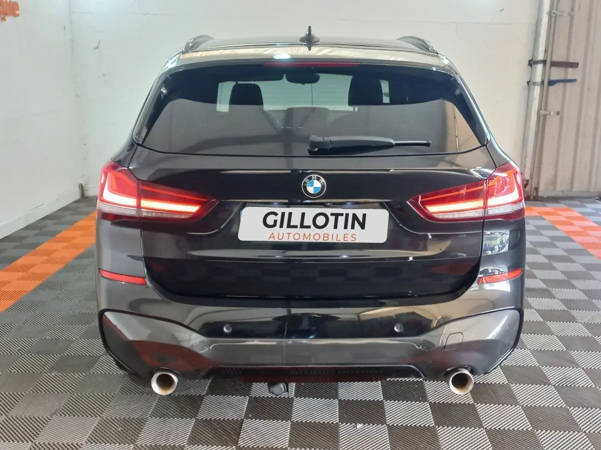 Vue arrière d'un BMW X1 xDrive20d noir 2022 avec feux LED allumés et double sortie d'échappement visible.