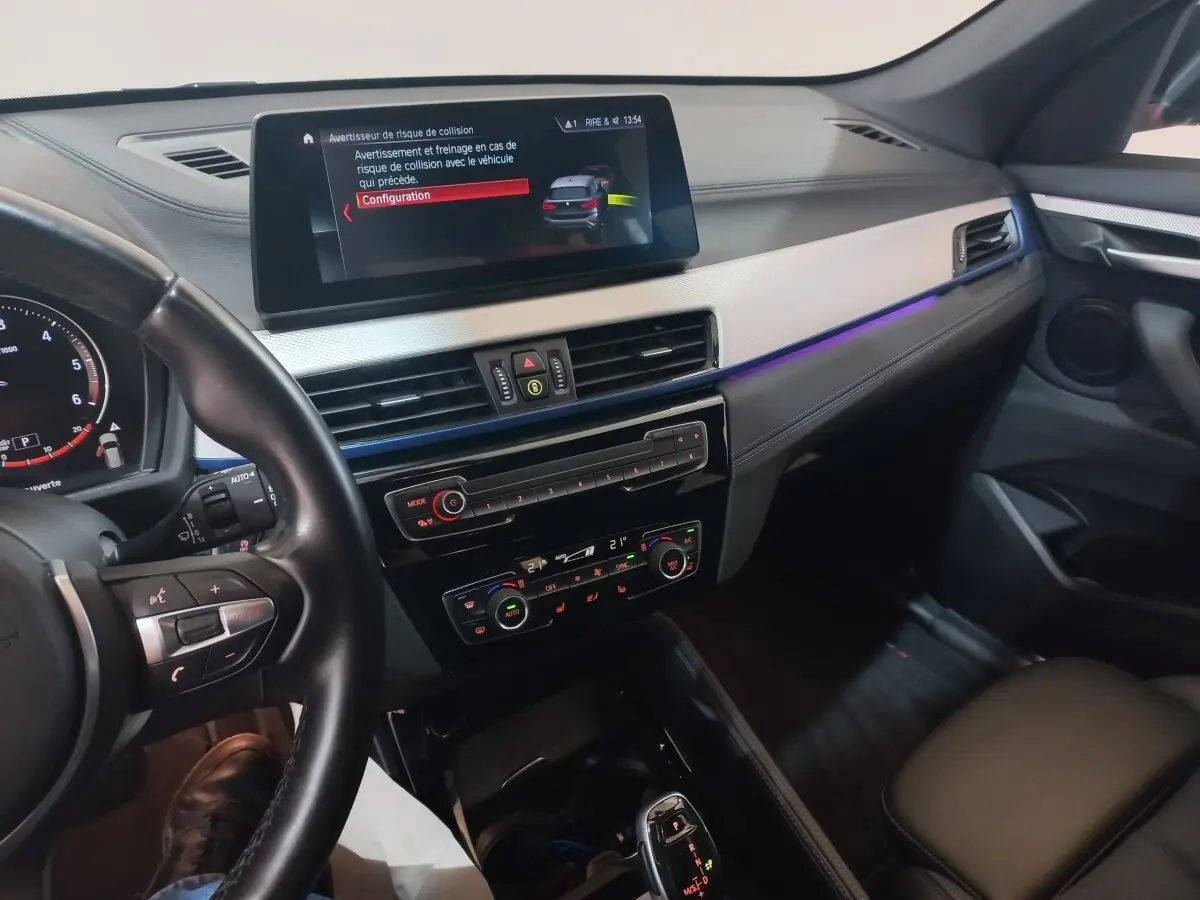 Vue intérieure côté conducteur du tableau de bord et écran tactile d'une BMW X1 noire, avec éclairage d'ambiance violet.