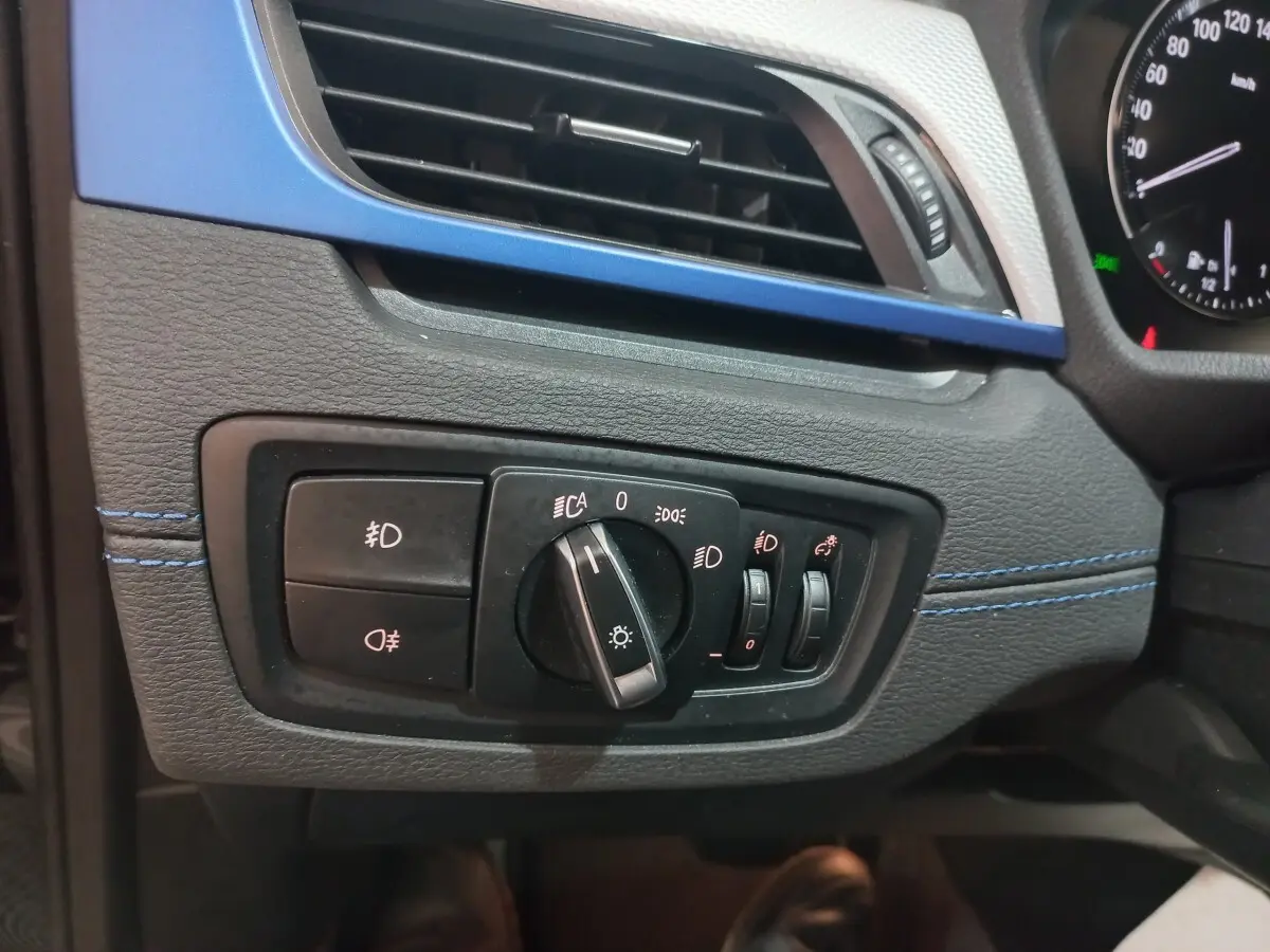 Détail du tableau de bord noir et bleu du BMW X1 2022, avec commandes d’éclairage et ventilation visibles.