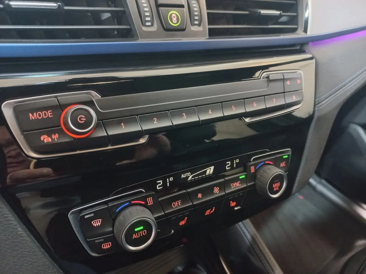 Gros plan sur la console centrale noire du BMW X1 xDrive20d M Sport 2022 avec commandes climatisation digitale et boutons lumineux.