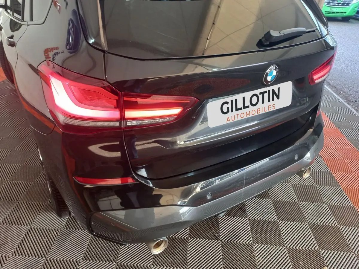 Vue 3/4 arrière droite d’un BMW X1 xDrive20d M Sport noir avec feux LED allumés et double sortie d’échappement chromée.