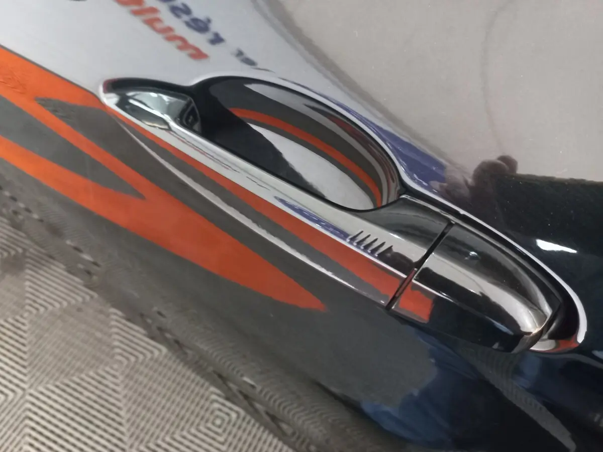 Poignée de porte noire brillante côté droit d’un BMW X1 xDrive20d M Sport 2022 avec reflet orange.