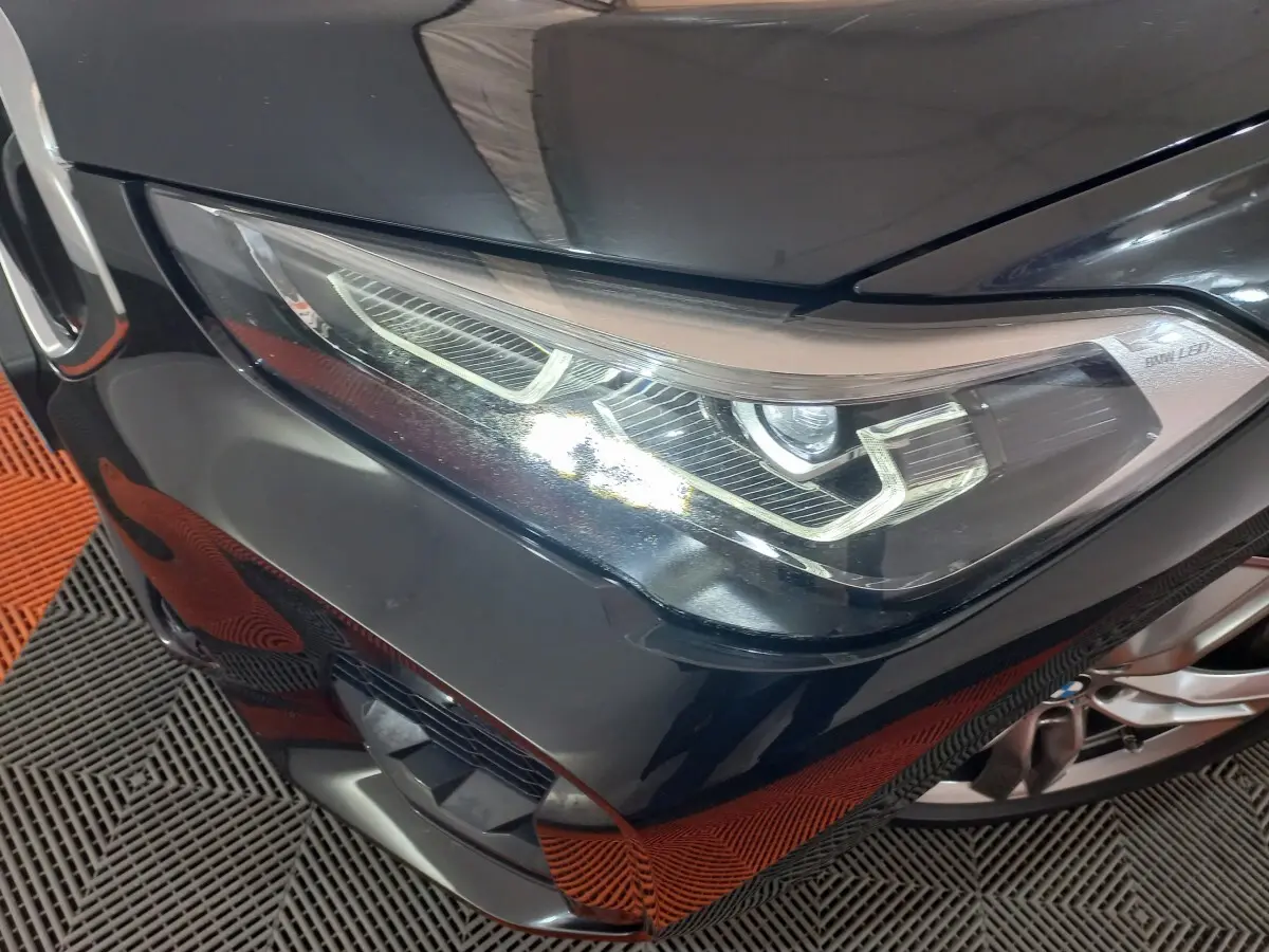 Gros plan sur le phare avant droit d’un BMW X1 noir, mettant en valeur les lignes LED distinctives et la calandre M Sport.