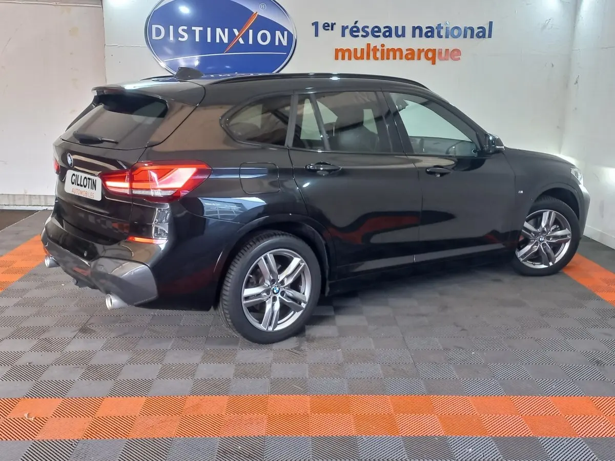 Vue 3/4 arrière droite d'un BMW X1 noir garé en intérieur avec jantes alliage et feux arrière allumés.