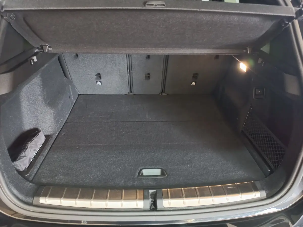Coffre ouvert vu de face d'un BMW X1 noir 2022, avec tapis noir et éclairage latéral intérieur allumé.