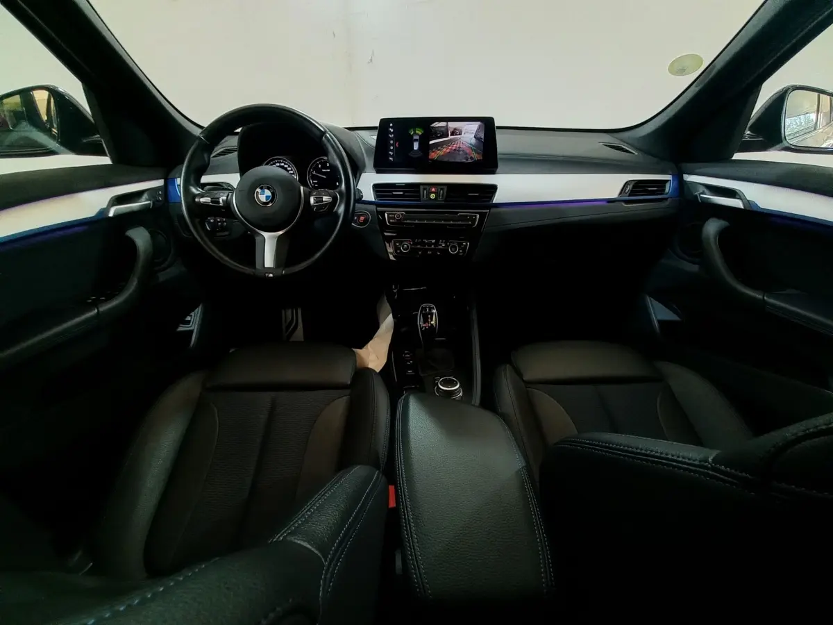 Vue intérieure avant du BMW X1 noir 2022, tableau de bord avec écran tactile et volant cuir multifonctions.