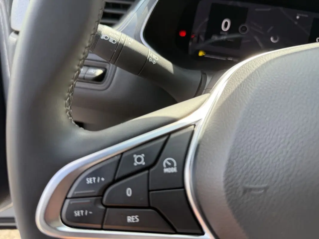 Gros plan sur les commandes au volant du Renault Captur 2025, avec boutons de régulateur et tableau de bord numérique en arrière-plan.