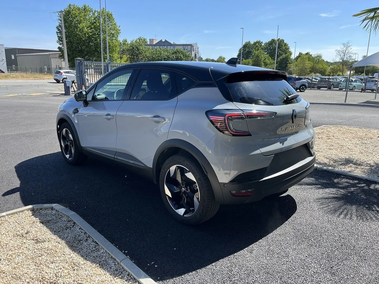 Renault Captur 2025 gris rafale avec toit noir, vu en 3/4 avant droit devant un bâtiment industriel.