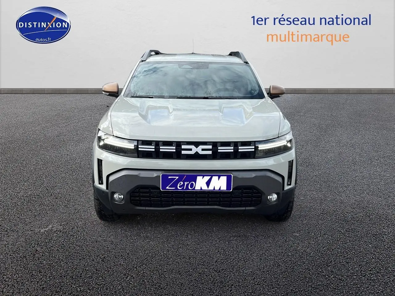 Vue frontale du Dacia Duster 2025 couleur Sandstone avec calandre noire et plaques Zero KM visibles.