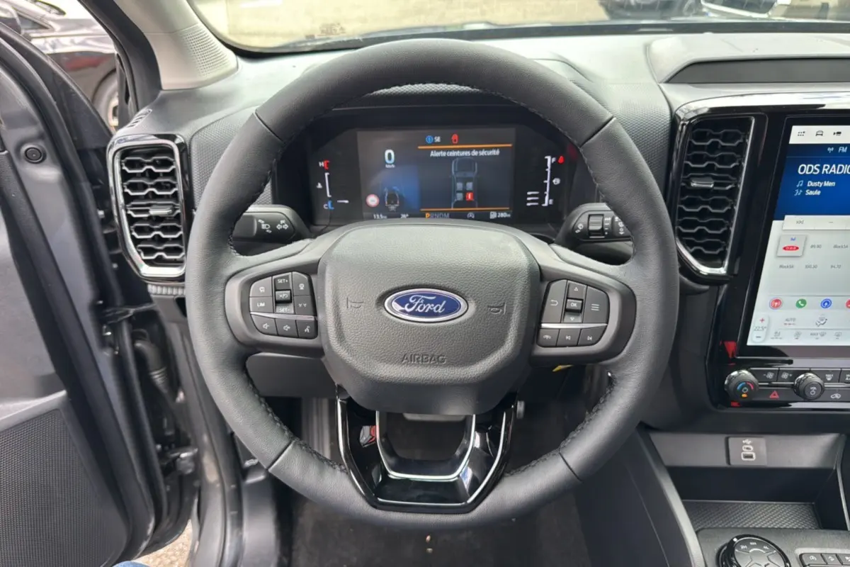 Vue centrée du volant noir du Ford Ranger 2025 gris carbone, avec tableau de bord digital et écran tactile visible.