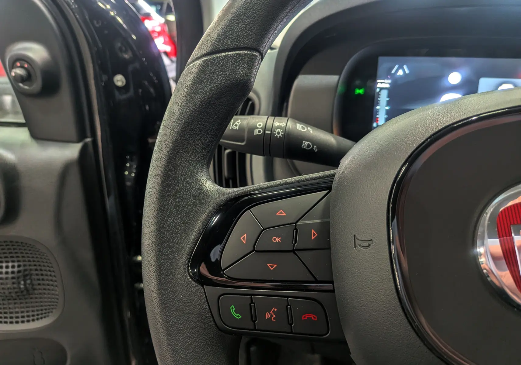 Gros plan sur le volant noir de la FIAT Panda 2025 hybride, montrant les commandes intégrées et le tableau de bord numérique.