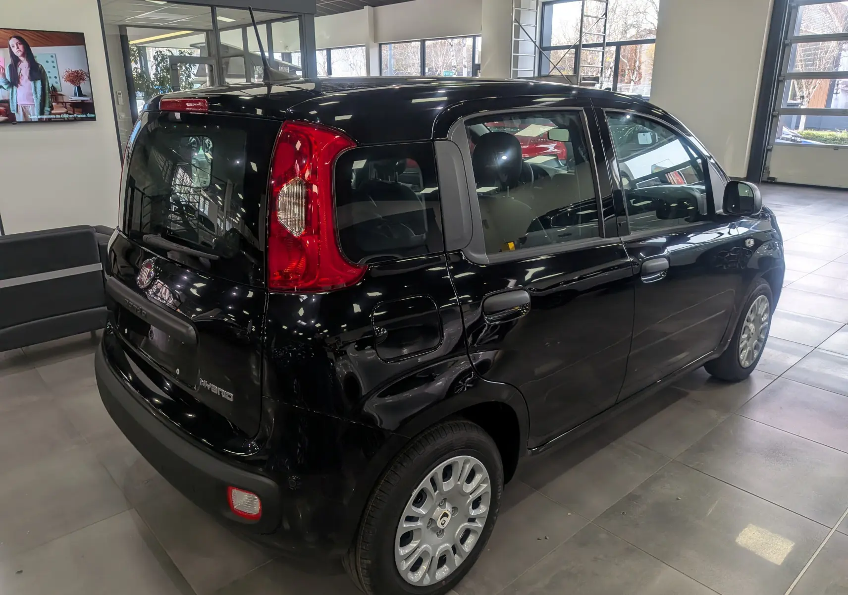 Vue 3/4 arrière droite d'une FIAT Panda 1.0 Hybrid 2025 noir brillant en showroom avec feux arrière rouges.