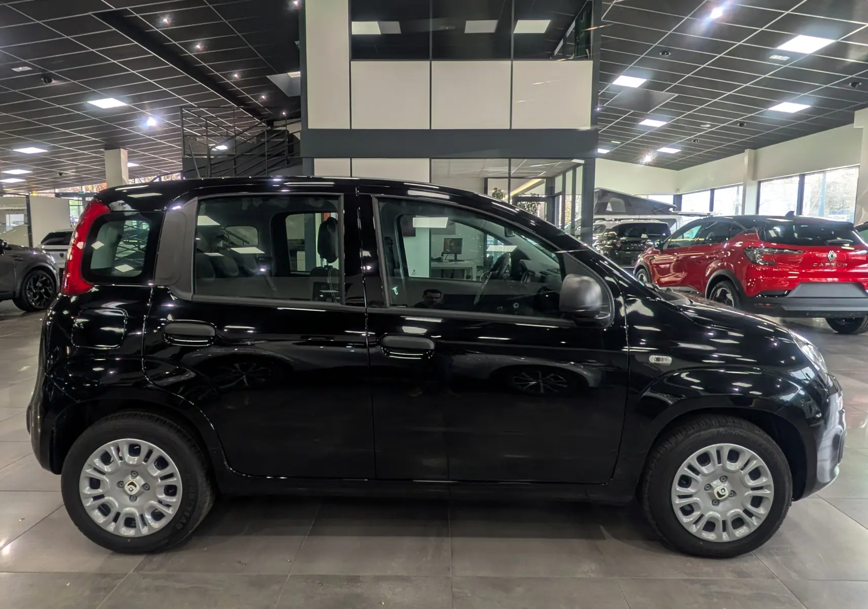 Profil côté droit de la Fiat Panda 1.0 70 CH Hybrid City noire, en intérieur de showroom lumineux.
