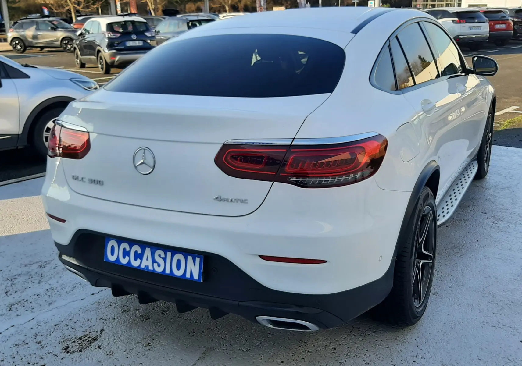 Vue 3/4 arrière droite d'un Mercedes GLC Coupé blanc avec feux LED et jantes noires sur parking.