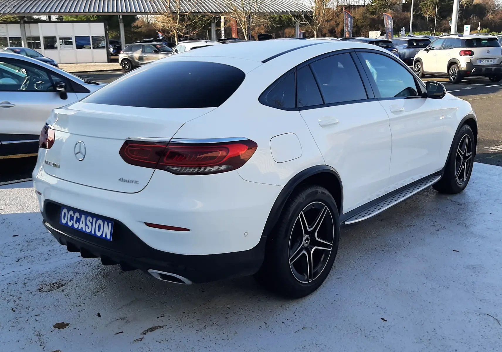 Vue 3/4 arrière droite d'un Mercedes GLC Coupé 300 4MATIC blanc avec jantes AMG noires et vitres teintées.