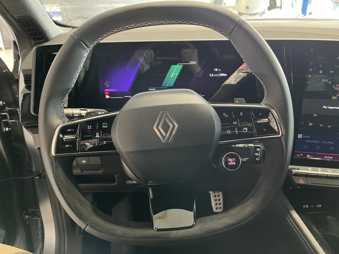 Vue rapprochée du volant noir avec surpiqûres bleues et écran numérique du tableau de bord du Renault Austral hybride 2025.