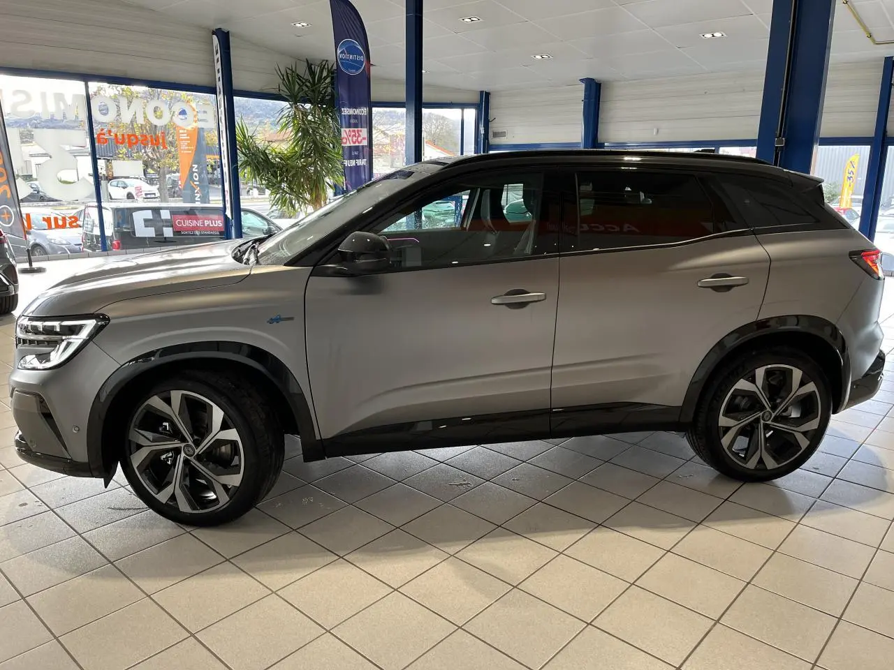 Vue latérale droite du Renault Austral gris avec toit noir étoilé et jantes alliage 20 pouces dans un showroom.