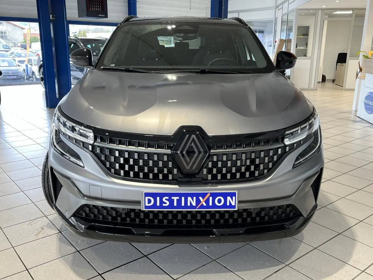 Vue avant d’un Renault Austral gris avec calandre à damier noire et logo Alpine, en showroom intérieur.