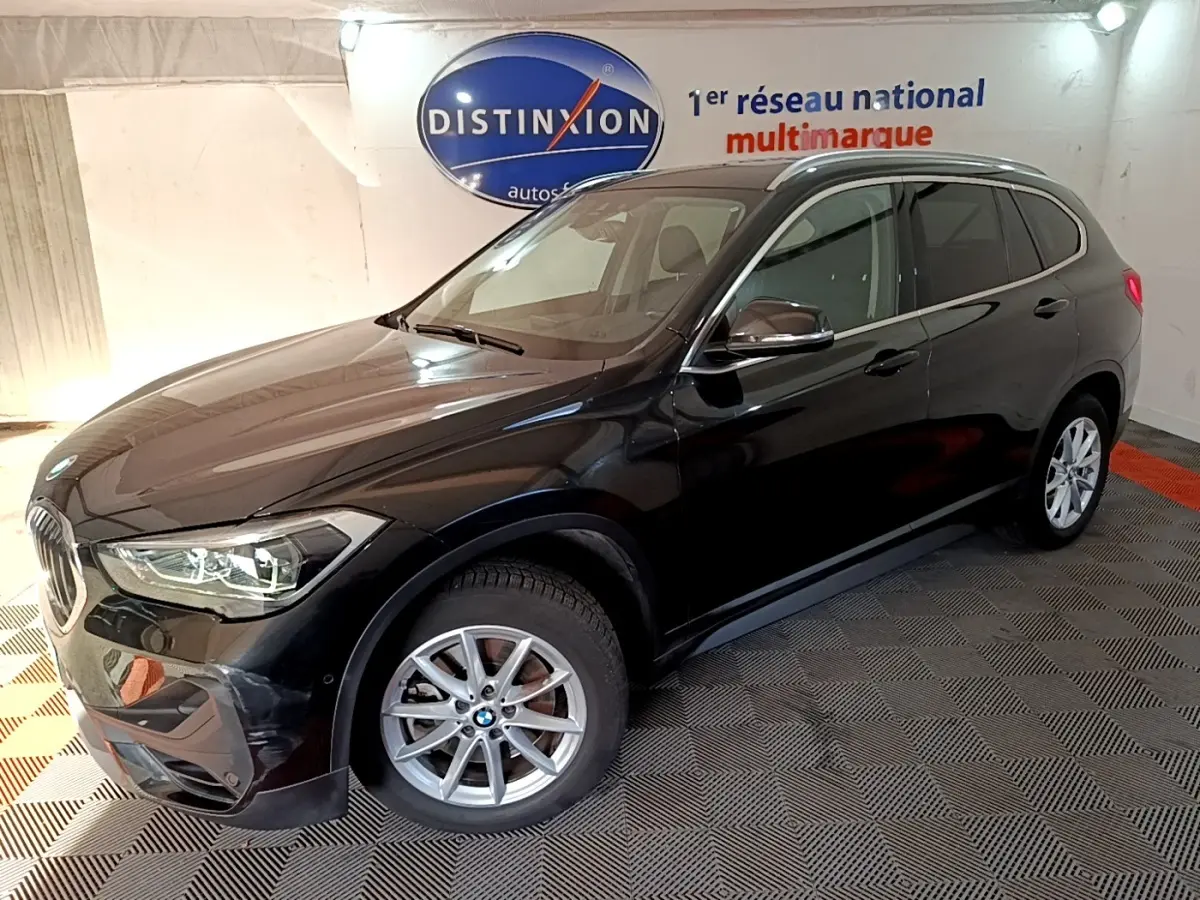 BMW X1 sDrive20i noir vue 3/4 avant droit en intérieur avec jantes alliage et phares LED allumés