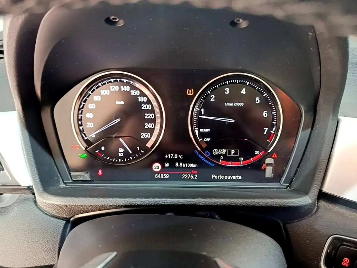 Vue rapprochée du tableau de bord numérique du BMW X1 noir, affichant vitesse, compte-tours et alertes.