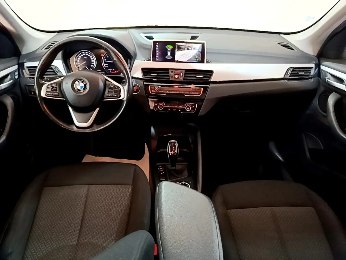 Vue intérieure avant du tableau de bord et volant cuir noir d'une BMW X1 sDrive20i avec écran tactile et boîte automatique.